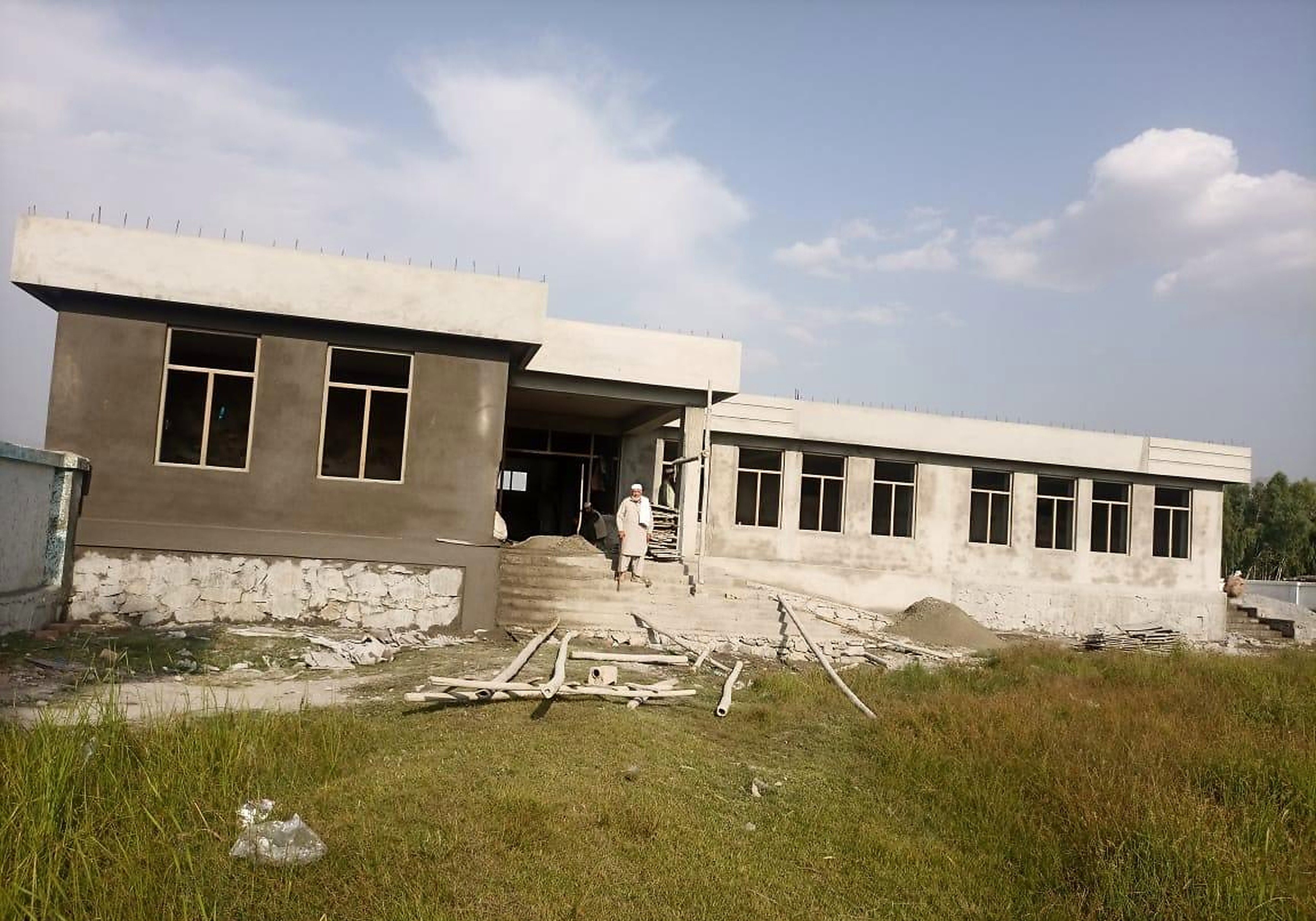 The new school building under construction, with plastered walls, a concrete roof slab, and window frames installed